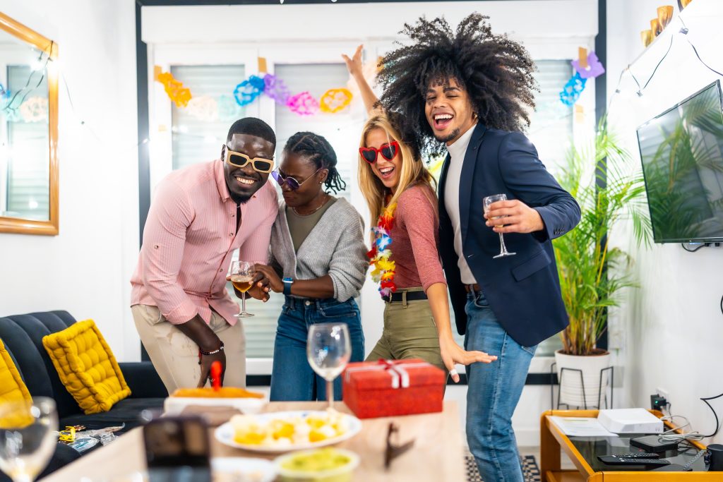Happy young friends of different ethnicity dancing during home birthday party