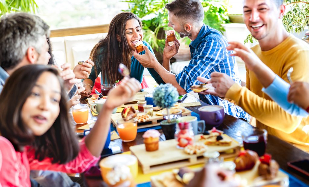 Happy friends eating and drinking at coffee bar garden - Young people having fun together at cafeteria on brunch time - Life style concept with cool men and women at cafe venue - Bright vivid filter