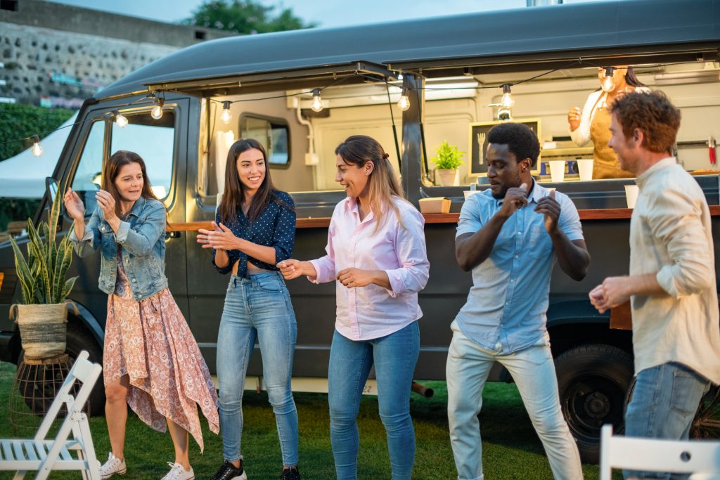 Group of multiethnic friends in casual clothes standing near van and chatting while spending time together