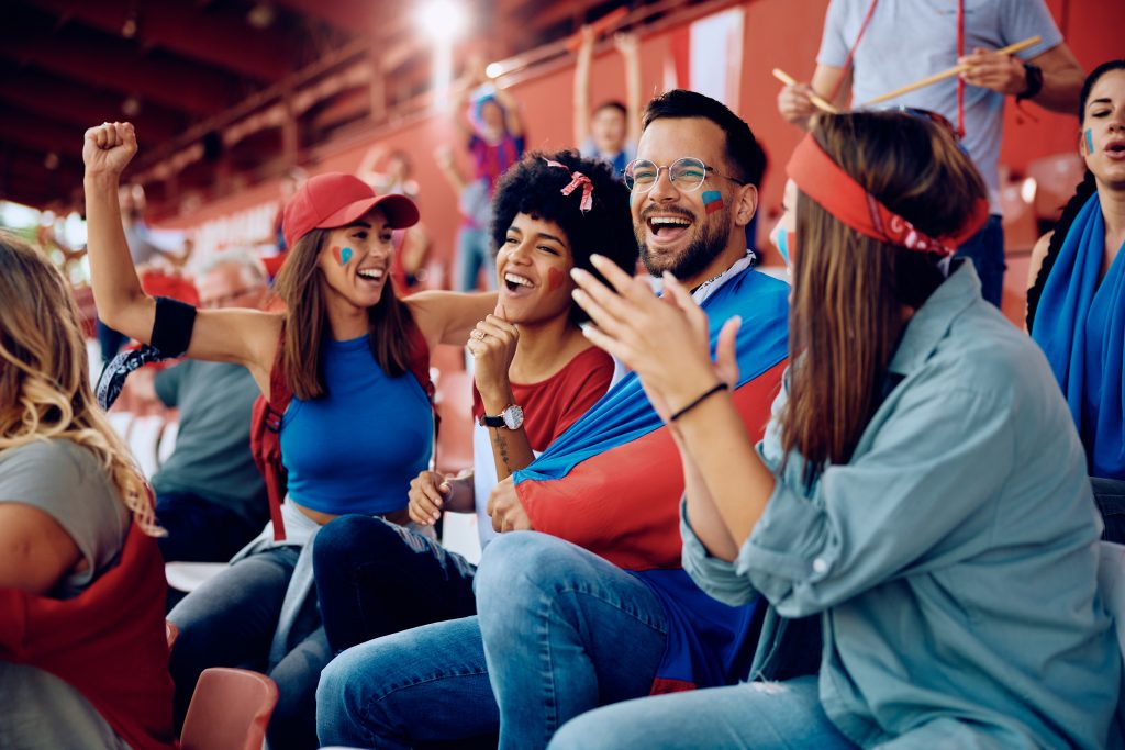 Multiracial group of cheerful friends celebrating during sports game at the stadium.