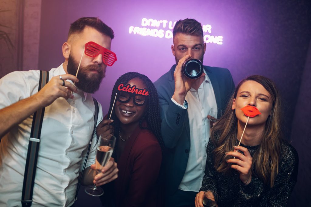 Happy group of friends dancing on a party in a club while drinking champagne and using funny face props