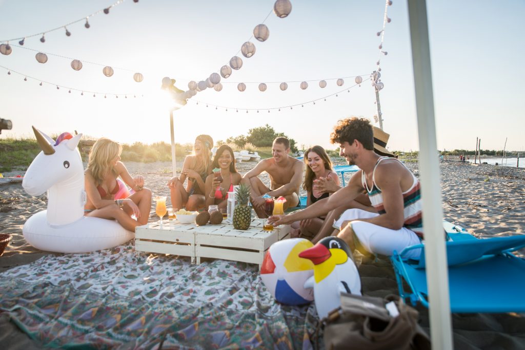 Group of friends having a picnic at the beach - Happy young people on a summer vacation at the beach