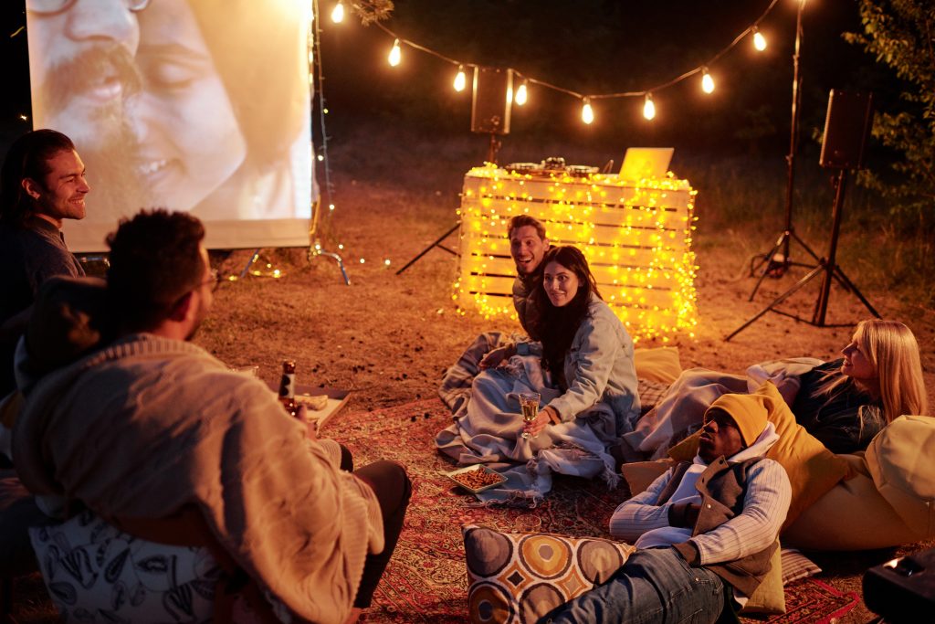 Group of young restful intercultural men and women in casualwear sitting and lying on carpet and pillows while having drinks and snacks