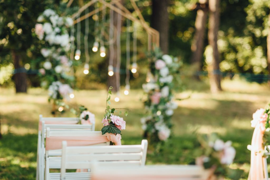 A wedding ceremony with white chairs and bright pink flowers in the lush green grass
