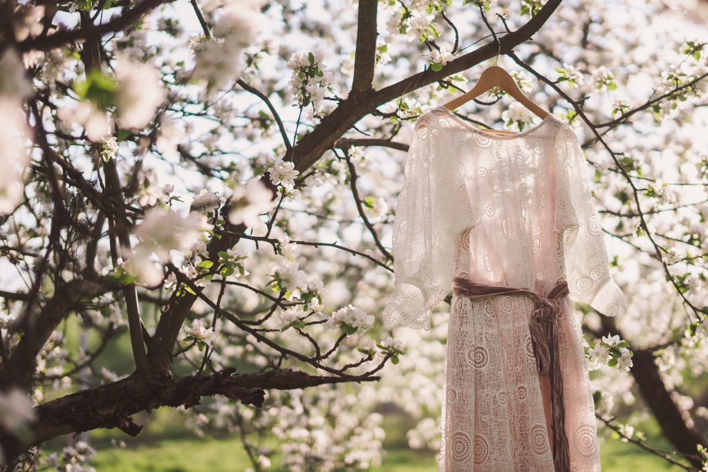 Beautiful lace dress hanging on the blooming tree in spring garden on sunset