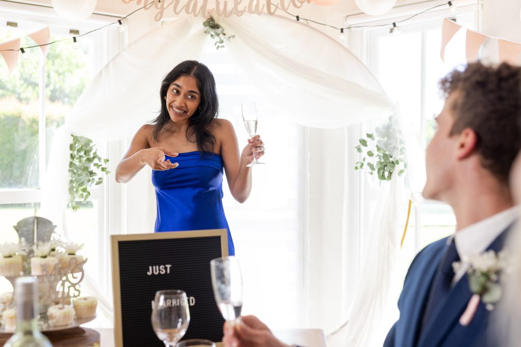 Woman in blue dress giving toast at wedding reception, smiling and holding champagne. Celebration, party, happiness, formal wear, evening dress, occasion