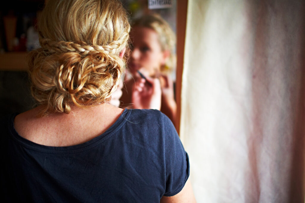 Blonde woman with plaits applying make up in mirror