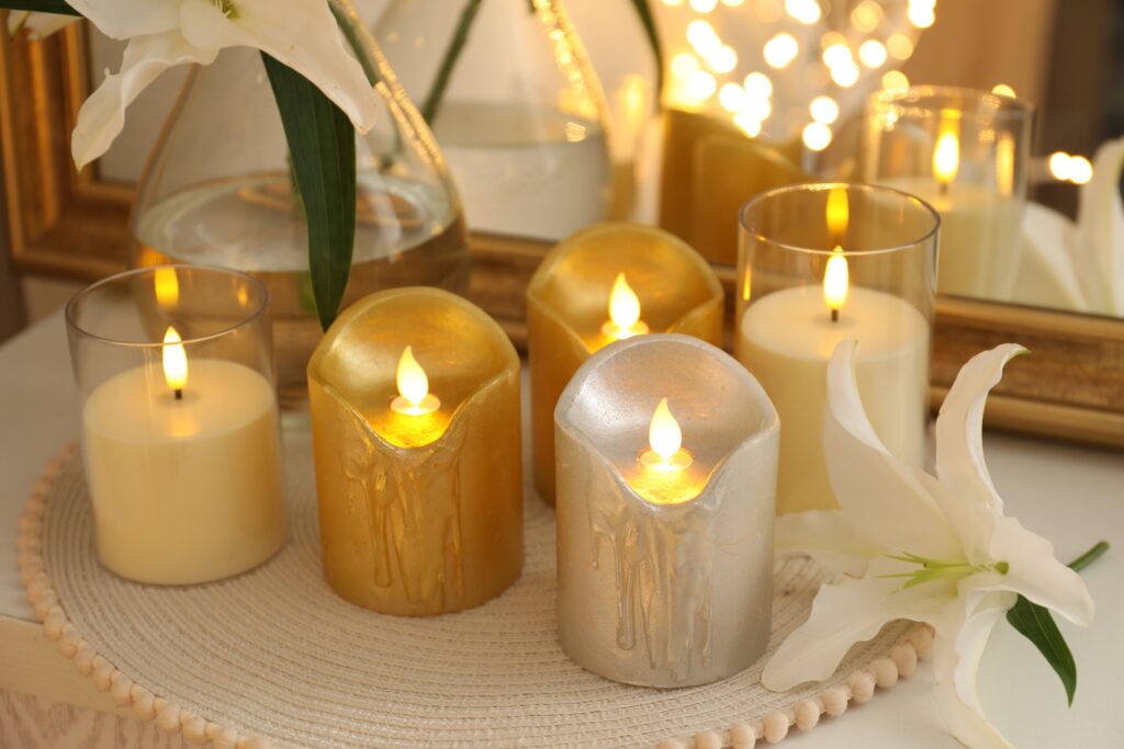 Beautiful LED candles and lily flowers near mirror on light table indoors, closeup. Bokeh effect