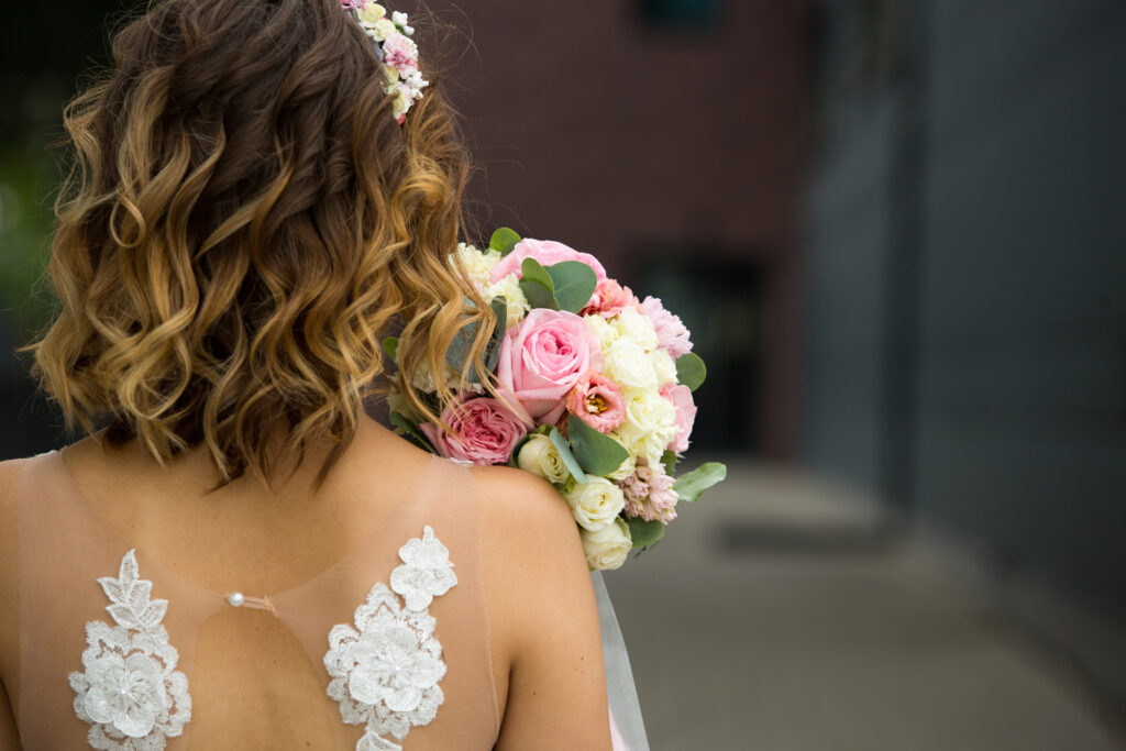 Back of the bride in a white wedding dress close-up. Bride's bouquet of roses in pastel colors, curls. Angel wings in the decoration of the dress. Bride fees, wedding ceremony. Space for text
