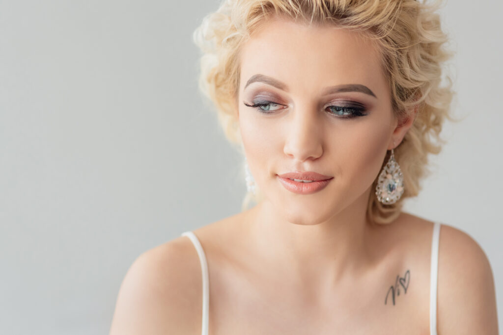 Beautiful young woman with a trendy blonde hairstyle, head and shoulders portrait on a grey studio background