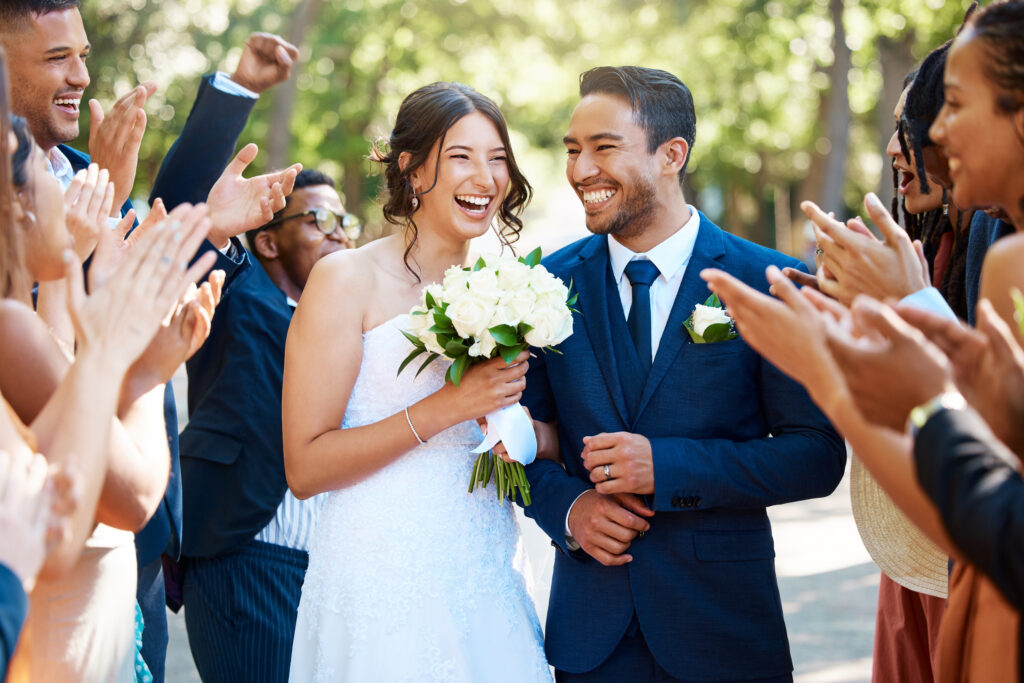 Wedding guests clapping hands as the newlywed couple walk down the aisle. Joyful bride and groom wa.