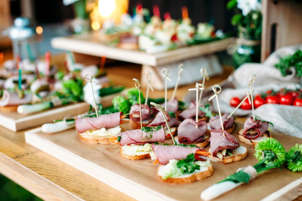 Delicious catering banquet buffet table decorated in rustic style in the garden. Different snacks, sandwiches with ham and pesto sauce. Outdoor, closeup.