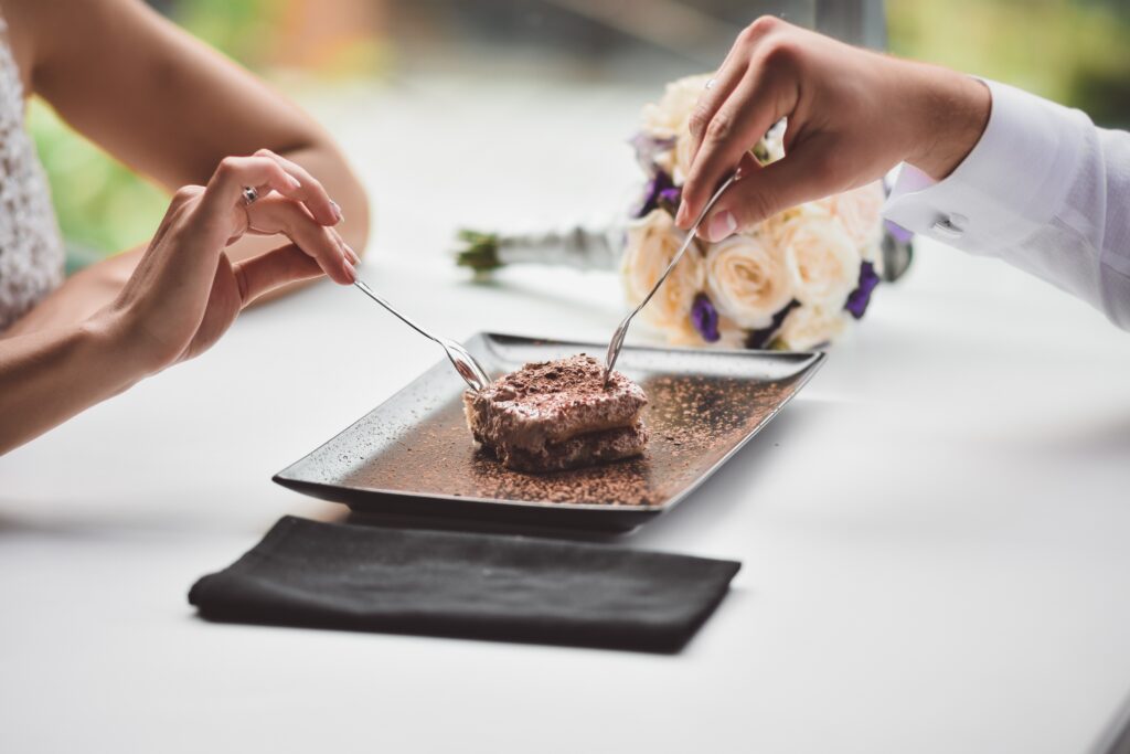 A man and a young girl eat a cake. A date in a cafe. A bouquet of flowers in the background in defocus. Hands close-up. Without a face. Meeting of lovers in a restaurant.