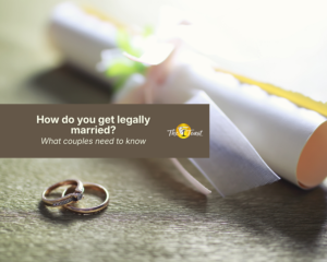 how-do-you-get-legally-married - two gold wedding rings beside a rolled certificate tied with ribbon on a wooden table