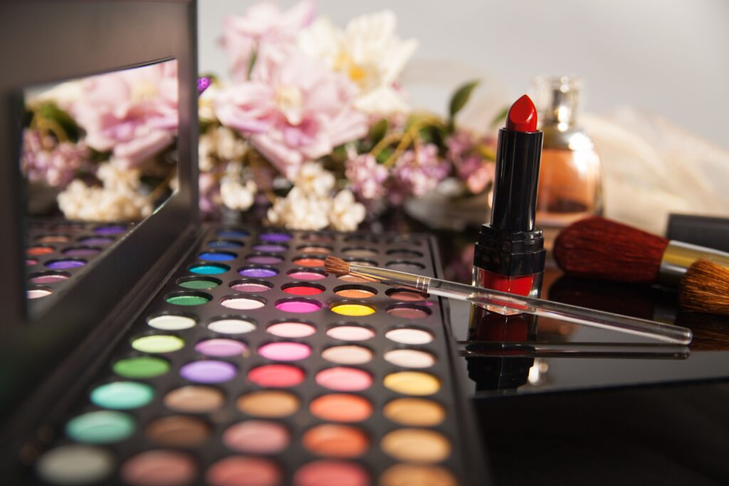 A colorful eye shadow palette and a red lipstick with flowers in the background